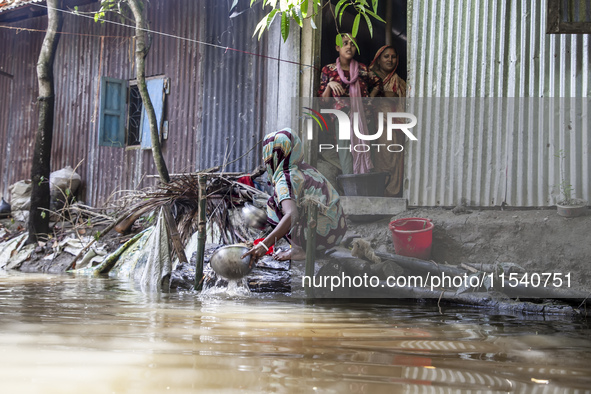 A woman washes essential items in floodwaters in front of her house in Sonapur Union of Sonaimuri Upazila of Noakhali District of Chittagong...