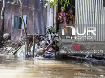 A woman washes essential items in floodwaters in front of her house in Sonapur Union of Sonaimuri Upazila of Noakhali District of Chittagong...