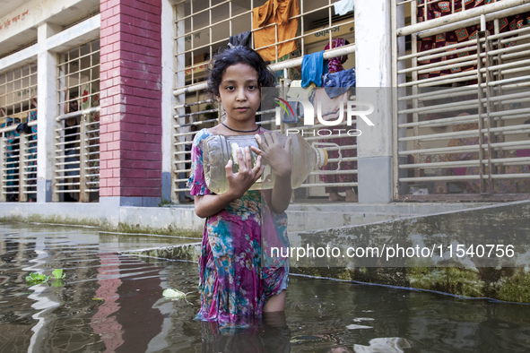 A child stands in flood waters in front of a shelter holding a drinking water bottle in Noakhali, Bangladesh, on September 2, 2024. 