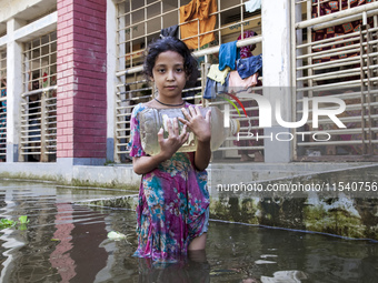 A child stands in flood waters in front of a shelter holding a drinking water bottle in Noakhali, Bangladesh, on September 2, 2024. (