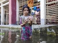 A child stands in flood waters in front of a shelter holding a drinking water bottle in Noakhali, Bangladesh, on September 2, 2024. (