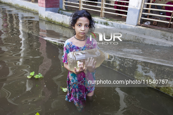 A child stands in flood waters in front of a shelter holding a drinking water bottle in Noakhali, Bangladesh, on September 2, 2024. 