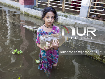 A child stands in flood waters in front of a shelter holding a drinking water bottle in Noakhali, Bangladesh, on September 2, 2024. (