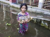 A child stands in flood waters in front of a shelter holding a drinking water bottle in Noakhali, Bangladesh, on September 2, 2024. (