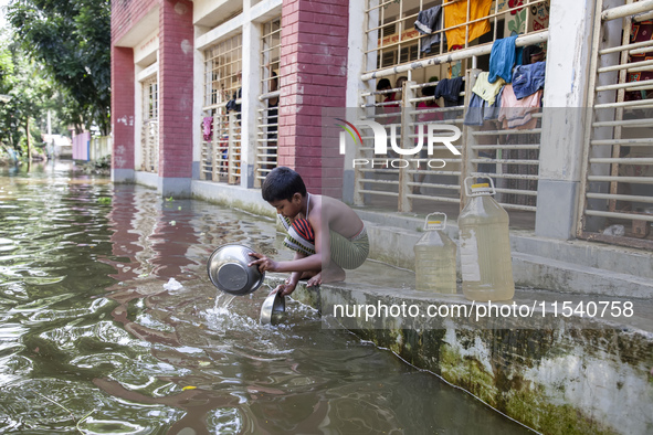 A child washes dishes in flood water in front of a shelter in Sonapur Union, Sonaimuri Upazila, Noakhali District, Chittagong Division, Bang...