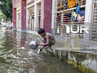 A child washes dishes in flood water in front of a shelter in Sonapur Union, Sonaimuri Upazila, Noakhali District, Chittagong Division, Bang...