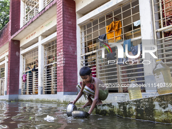 A child washes dishes in flood water in front of a shelter in Sonapur Union, Sonaimuri Upazila, Noakhali District, Chittagong Division, Bang...