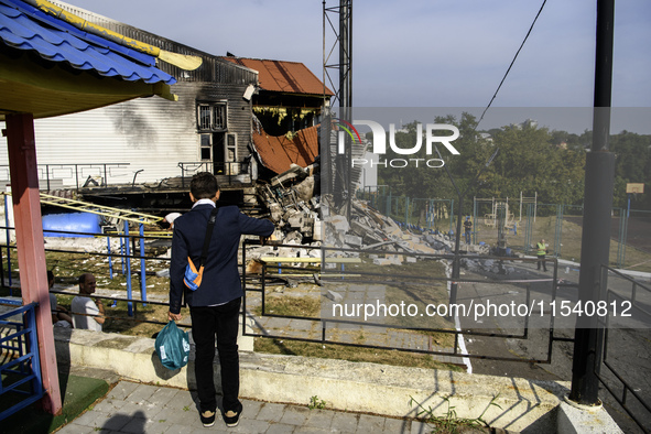 A schoolboy who comes to celebrate the beginning of the educational year stands near the sports complex of a university, a heavily damaged a...