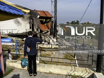 A schoolboy who comes to celebrate the beginning of the educational year stands near the sports complex of a university, a heavily damaged a...