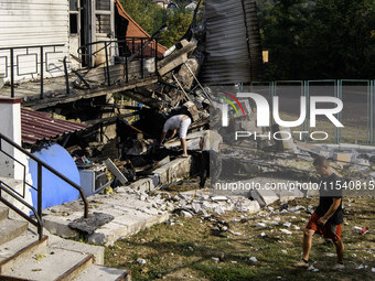 People work near the sports complex of a university with a heavily damaged and partially collapsed building after the Russian missile attack...