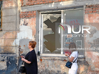 Two women walk past a window broken by the shock wave from the Russian missile attack in the Zaliznychnyi district of Lviv, Ukraine, on Sept...