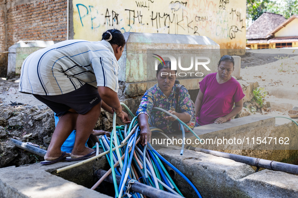 Residents fetch water from the only source by sucking it up and flowing it through a hose to their house during the drought season in Selopa...