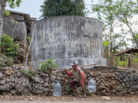 A villager carries water containers after collecting water for needs at his house during the drought season in Tepus Village, Gunung Kidul R...