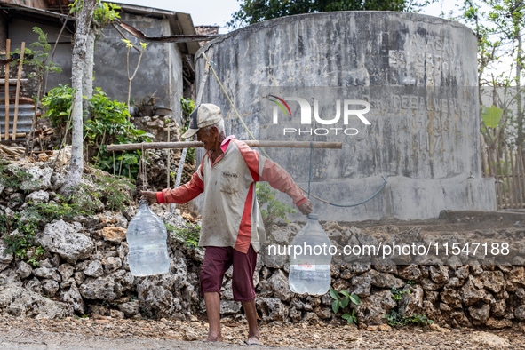 A villager carries water containers after collecting water for needs at his house during the drought season in Tepus Village, Gunung Kidul R...