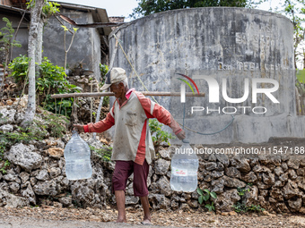 A villager carries water containers after collecting water for needs at his house during the drought season in Tepus Village, Gunung Kidul R...