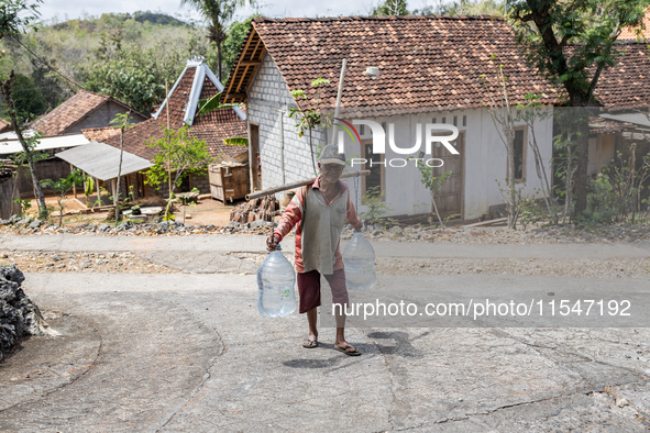 A villager carries water containers after collecting water for needs at his house during the drought season in Tepus Village, Gunung Kidul R...