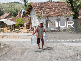 A villager carries water containers after collecting water for needs at his house during the drought season in Tepus Village, Gunung Kidul R...