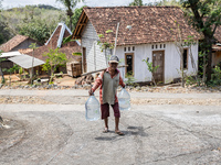 A villager carries water containers after collecting water for needs at his house during the drought season in Tepus Village, Gunung Kidul R...