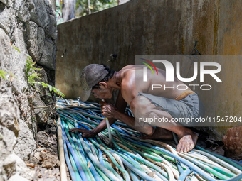 A man takes water from the only source of water by sucking it up and flowing it through a hose to his house during drought season in Selopam...