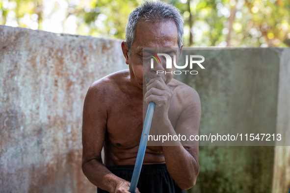 Sarjono (73), an elderly blind man, takes water from the only source of water by sucking it up and flowing it through a hose to his house du...