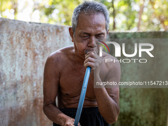 Sarjono (73), an elderly blind man, takes water from the only source of water by sucking it up and flowing it through a hose to his house du...