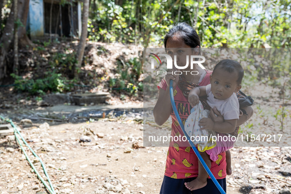 Desi (27) carries Tiffany, her child, while taking water from the only source of water by sucking it up and flowing it through a hose to her...