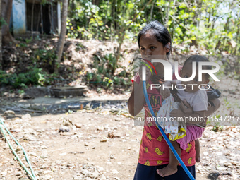 Desi (27) carries Tiffany, her child, while taking water from the only source of water by sucking it up and flowing it through a hose to her...