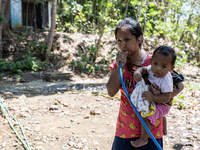 Desi (27) carries Tiffany, her child, while taking water from the only source of water by sucking it up and flowing it through a hose to her...