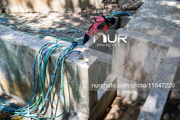 Desi (27) carries Tiffany, her child, while taking water from the only source of water by sucking it up and flowing it through a hose to her...