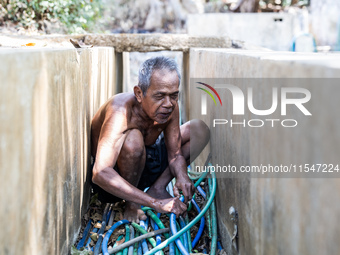 Sarjono (73), an elderly blind man, connects a water hose to the only water source to his house during the drought season in Selopamioro Vil...