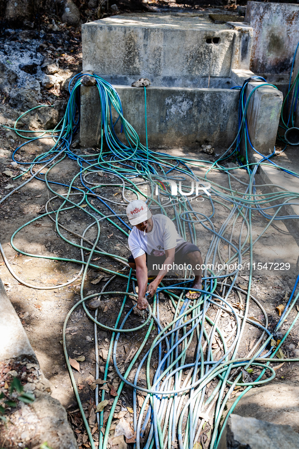 A man takes water from the only source of water by sucking it up and flowing it through a hose to his house during drought season in Selopam...