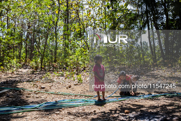 Desi (27) carries Tiffany, her child, while taking water from the only source of water by sucking it up and flowing it through a hose to her...