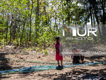 Desi (27) carries Tiffany, her child, while taking water from the only source of water by sucking it up and flowing it through a hose to her...