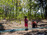 Desi (27) carries Tiffany, her child, while taking water from the only source of water by sucking it up and flowing it through a hose to her...