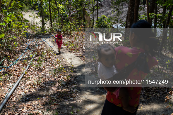 Desi (27) carries Tiffany, her child, while taking water from the only source of water by sucking it up and flowing it through a hose to her...