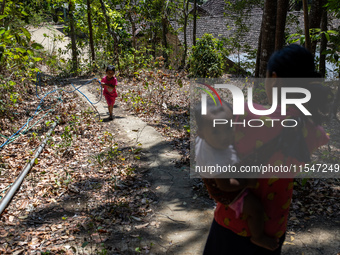 Desi (27) carries Tiffany, her child, while taking water from the only source of water by sucking it up and flowing it through a hose to her...