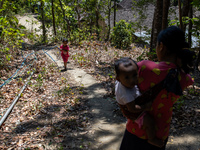 Desi (27) carries Tiffany, her child, while taking water from the only source of water by sucking it up and flowing it through a hose to her...