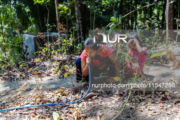 Desi (27) carries Tiffany, her child, while taking water from the only source of water by sucking it up and flowing it through a hose to her...