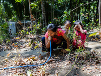 Desi (27) carries Tiffany, her child, while taking water from the only source of water by sucking it up and flowing it through a hose to her...