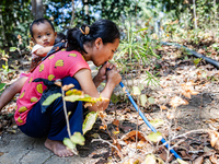 Desi (27) carries Tiffany, her child, while taking water from the only source of water by sucking it up and flowing it through a hose to her...