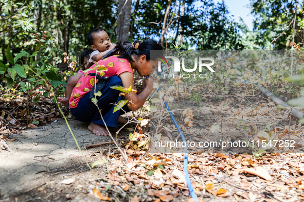 Desi (27) carries Tiffany, her child, while taking water from the only source of water by sucking it up and flowing it through a hose to her...