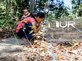 Desi (27) carries Tiffany, her child, while taking water from the only source of water by sucking it up and flowing it through a hose to her...