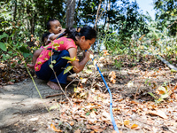 Desi (27) carries Tiffany, her child, while taking water from the only source of water by sucking it up and flowing it through a hose to her...