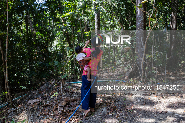 Desi (27) carries Tiffany, her child, while taking water from the only source of water by sucking it up and flowing it through a hose to her...