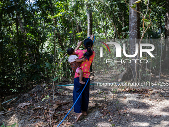 Desi (27) carries Tiffany, her child, while taking water from the only source of water by sucking it up and flowing it through a hose to her...