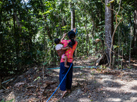 Desi (27) carries Tiffany, her child, while taking water from the only source of water by sucking it up and flowing it through a hose to her...