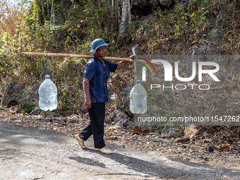 A villager carries water containers after collecting water for their livestock and plantation during the drought season in Tepus Village, Gu...