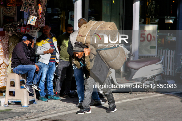 A laborer carries a heavy load along the Mall Road in Mussoorie, Uttarakhand, India, on April 18, 2024. 