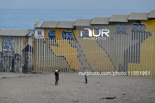 Two tourists take a selfie while posing near a new interactive mural of deported veterans at the Playas de Tijuana beach border wall, ''The...