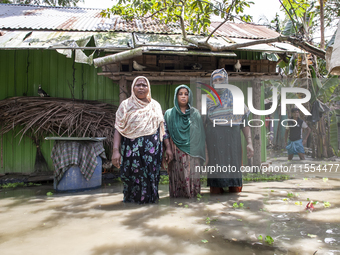 Three women stand in front of their flood-damaged houses in a village in Chaumuhni Municipality of Noakhali District, Chittagong Division, B...